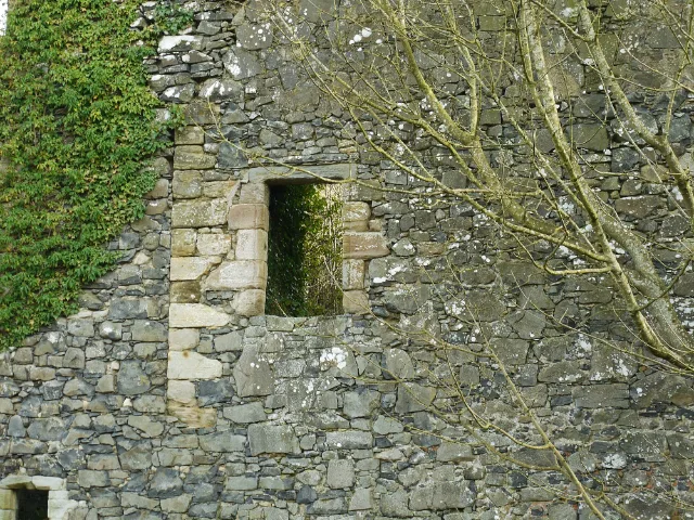 Empty window in Auchans Castle stone wall behind bare branches