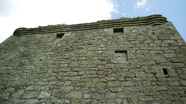 Blick nach oben auf die Steinmauer von Barr Castle, zugemauerte Öffnungen und die profilierte Brüstung.
