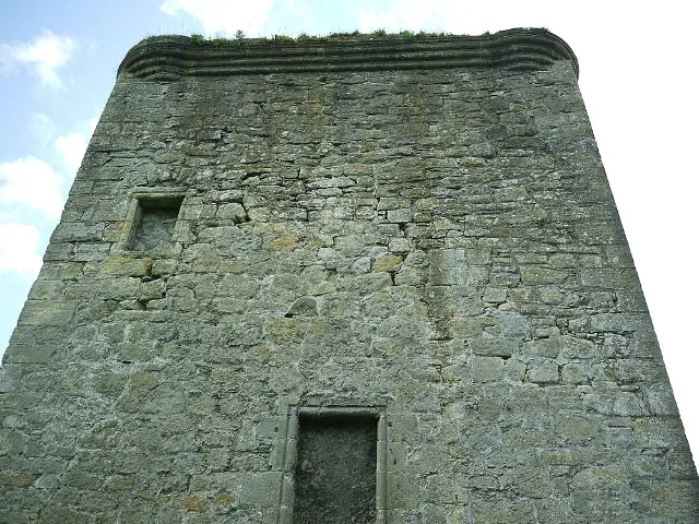 Blick nach oben auf eine verwitterte Mauer von Barr Castle mit zugemauerten Fenstern unter der Brüstung.