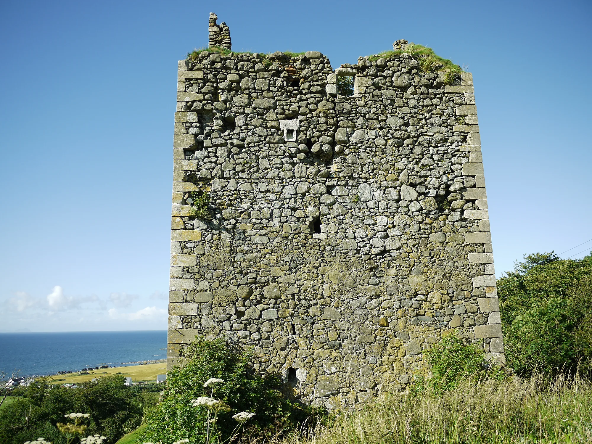 Stehende steinerne Turmwand von Carleton Castle über Meer und Küstengras